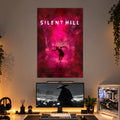 A large vertical wall art print featuring the 'Silent Hill' logo and a dark figure against a vivid pink and magenta misty forest scene, displayed above a desk setup with a monitor, keyboard, and PC tower in a modern room.